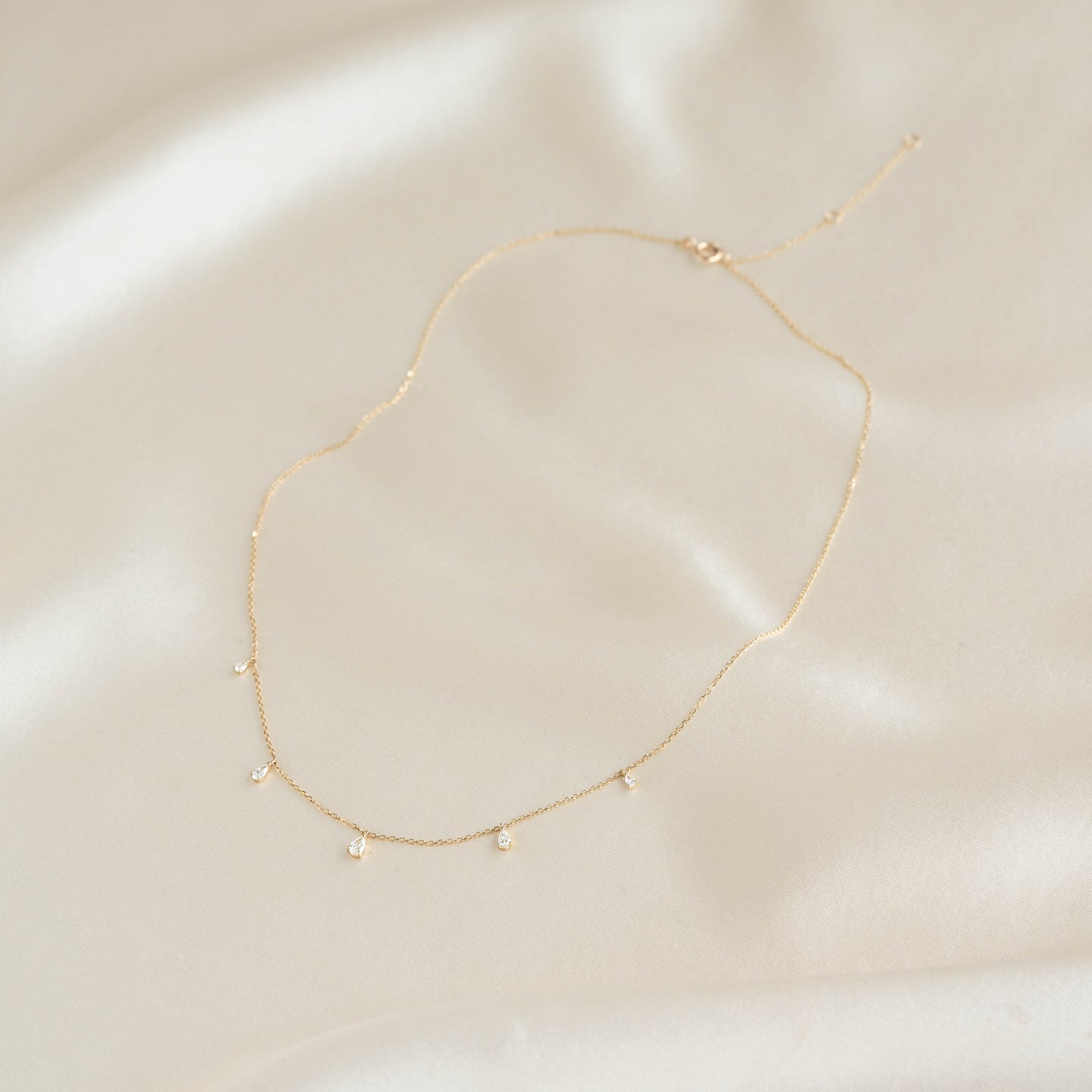 Pear Cut Diamond Pendant Necklace 14k Gold - Sylvie laid flat on cream fabric background in soft light