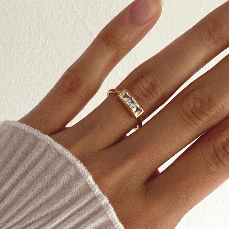 Close-up of a hand wearing a gold ring with two rectangular clear stones against a white background