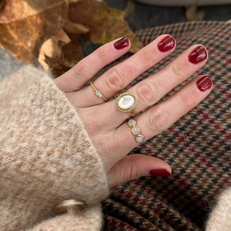 Close-up of a hand with burgundy nail polish wearing three gold rings on a patterned fabric background