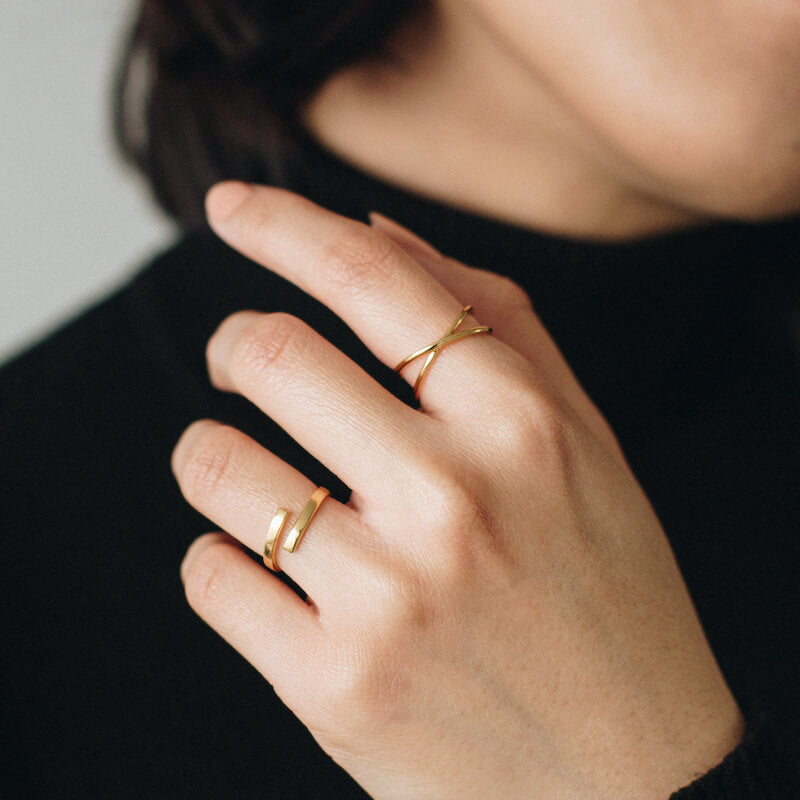 Close-up of a hand wearing two delicate gold rings on a black long-sleeve top background