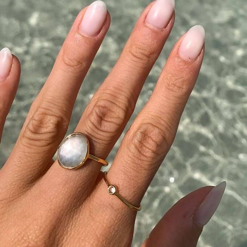 Close-up of a hand with well-manicured nails wearing two delicate gold rings over a softly blurred water background