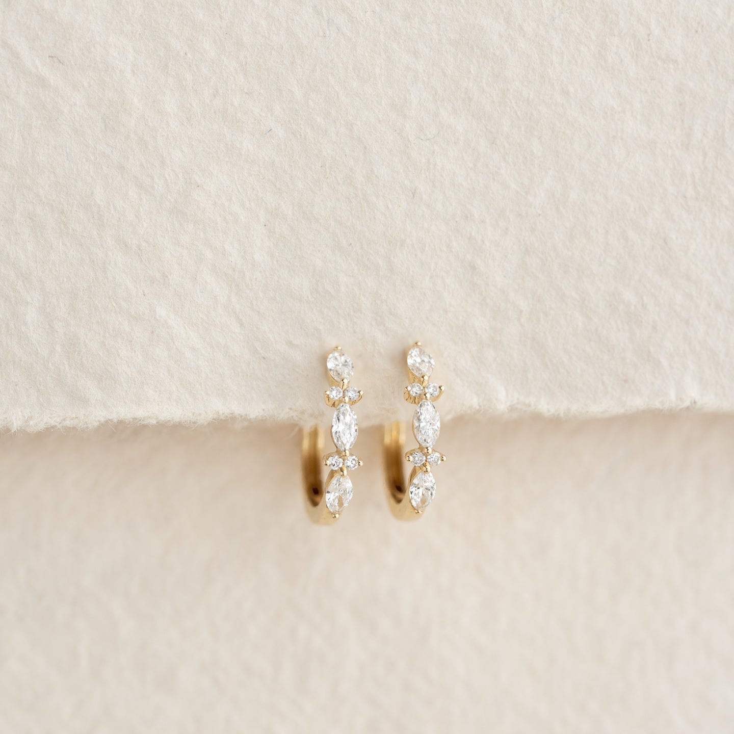 Close-up of Marquise and Round Diamond Huggie Earrings 14k Gold - Zoya on textured neutral background
