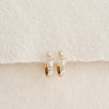 Close-up of Marquise and Round Diamond Huggie Earrings 14k Gold - Zoya on textured neutral background