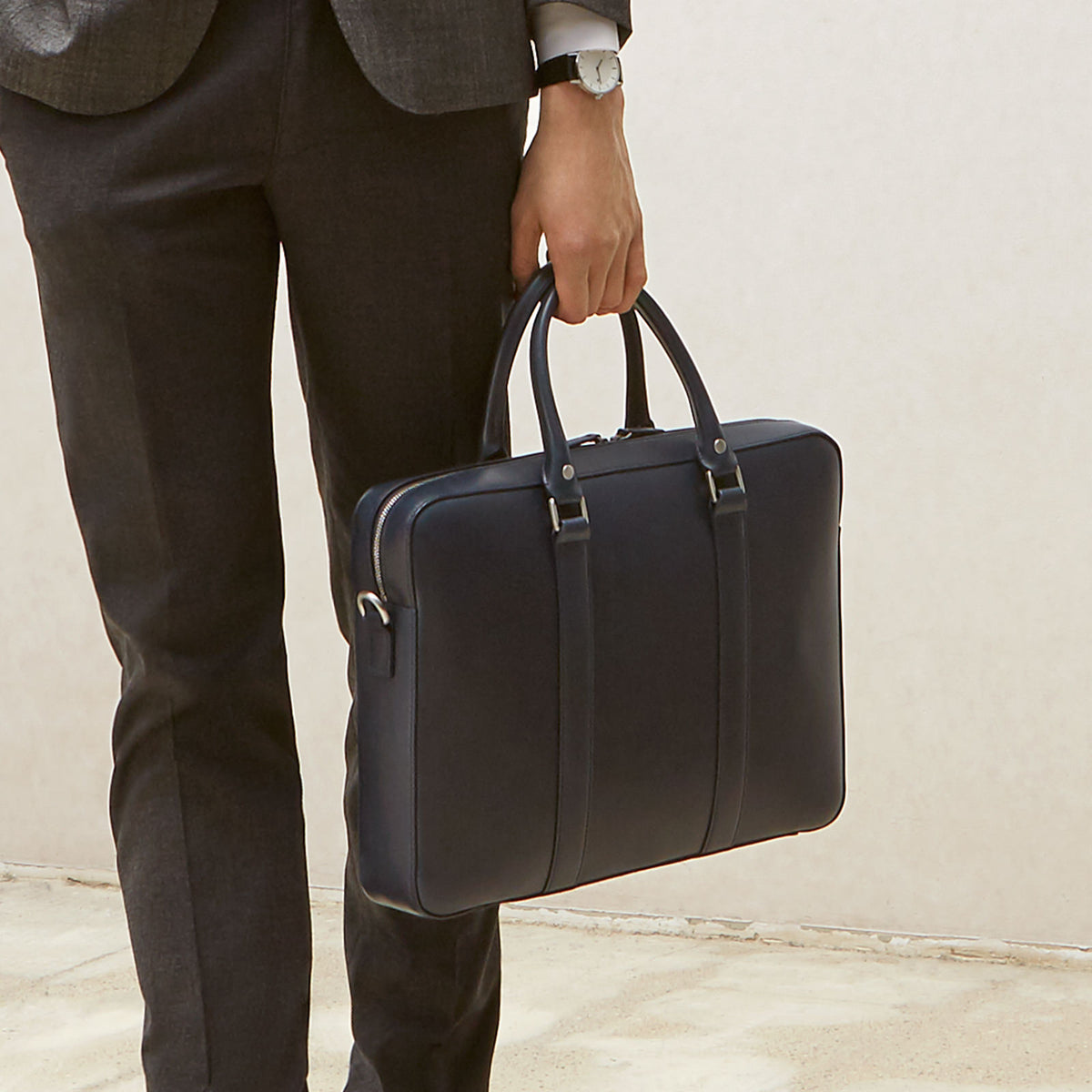 Man holding The Soft Briefcase (Private) in smooth leather with handles, shown with dark tailored pants and blazer