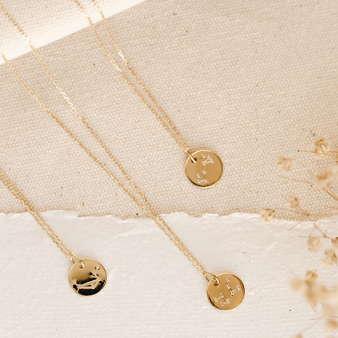 Zodiac necklaces in gold vermeil laying on textured background